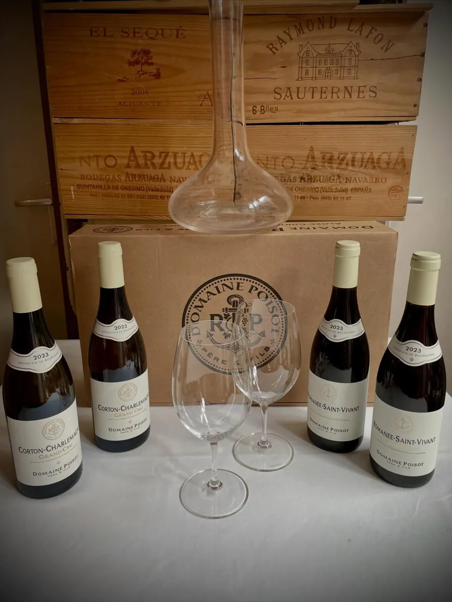 Flessen Corton-Charlemagne Grand Cru en Romanée-Saint-Vivant Grand Cru 2023 van Domaine Poisot op een gedekte tafel, met een karaf en twee wijnglazen, voor houten wijnkisten